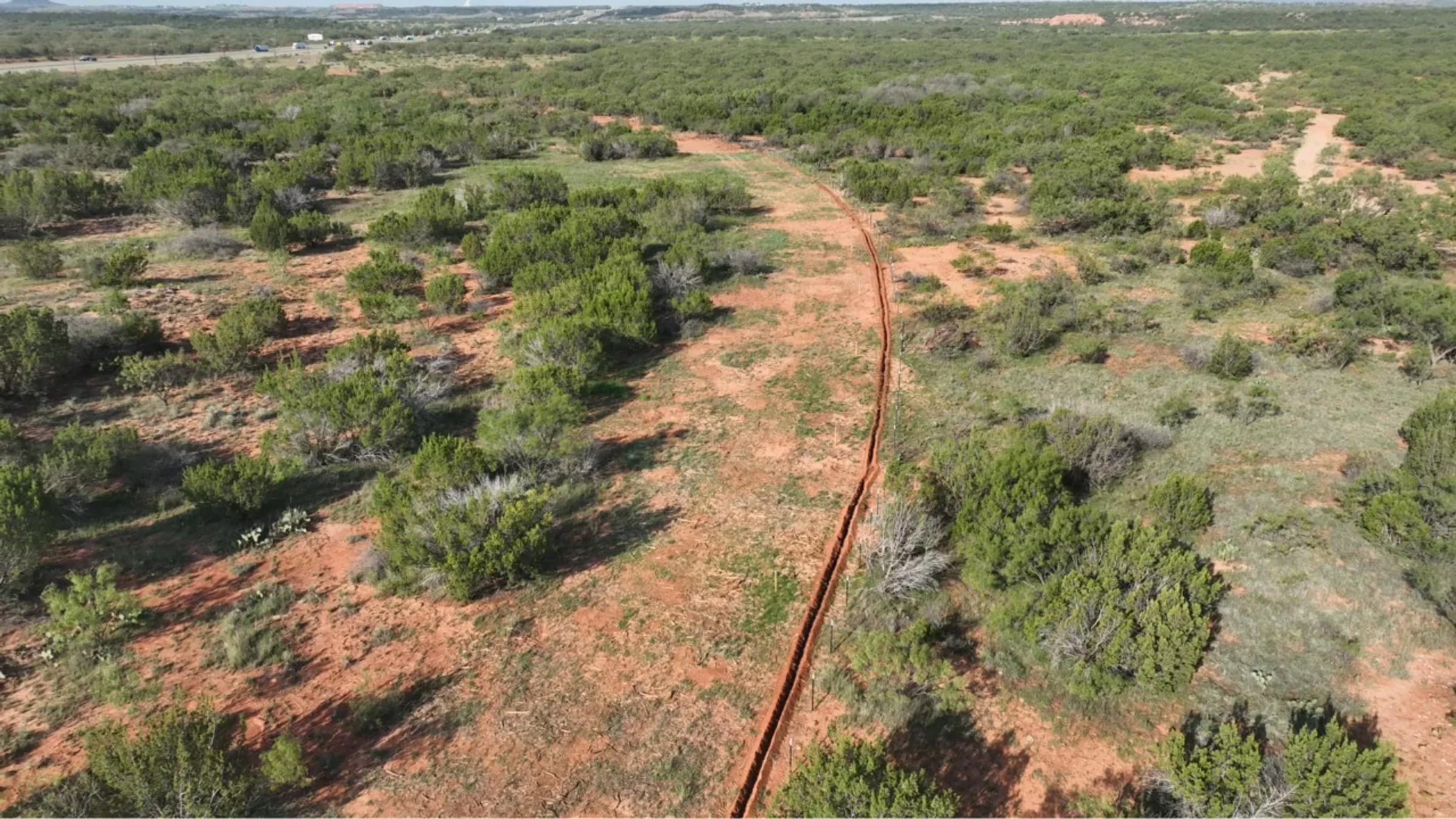 Low aerial view of a cleared pipeline corridor curving through West Texas brush.