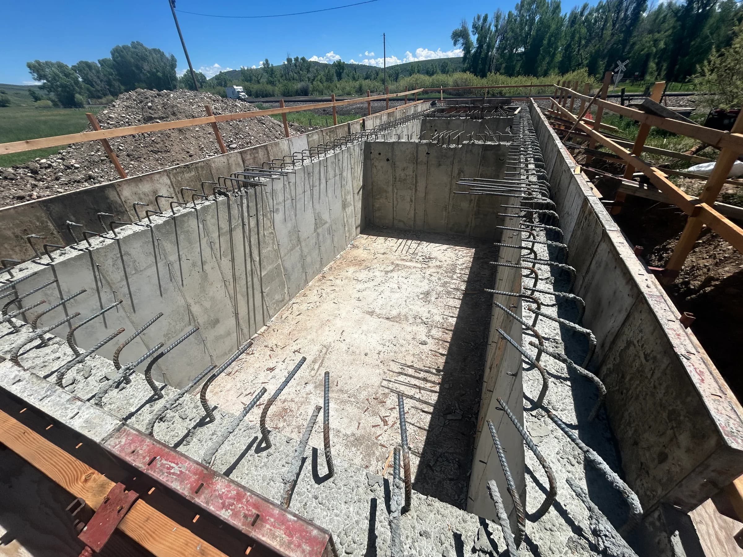 Cast-in-place concrete tank walls with rebar dowels and timber formwork under construction on a rural site